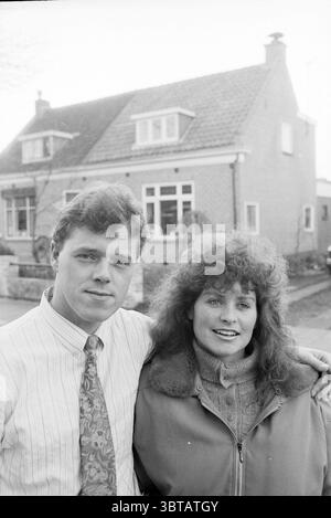 Family van Haaster Warmond Warmond, Whizgle News, Dutch Desk, Niederlande, 1950 - 2000 am 25-03-1991. Dies sind die Elemente im Bild. In einer vorstädtischen Umgebung steht ein junges Paar eng zusammen und steht im Vordergrund. Der Mann hat einen ordentlichen Haarschnitt und ist in einem Hemd mit Kragen mit vertikalem Streifenmuster und einer gemusterten Krawatte verziert, die ein poliertes Aussehen ausstrahlt. Sein Ausdruck ist ernst, aber warm, was auf einen Moment von Bedeutung hindeutet. Neben ihm besitzt eine Frau voluminöses, lockiges Haar, das ihr Gesicht wunderschön umrahmt. Sie trägt eine kuschelige Jacke mit Reißverschluss im Lagenlook Stockfoto