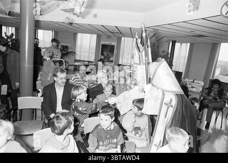 Sinterklaas on Haarlems Dagblad Haarlem the Netherlands, Whizgle News, Dutch Desk, Niederlande, 1950 - 2000 am 28-11-1995. Diese Themen sind in der Abbildung dargestellt. Die Szene spielt in einem hellen, geräumigen Raum voller verspielter Energie und Lachen. Kinder, eine Mischung aus Jungen und Mädchen, sitzen in mehreren Reihen von Holzstühlen, ihre Jugendlichen Gesichter sind ein Gobelin aus Neugier und Aufregung. Einige Kinder tragen farbenfrohe Kleidung, während andere gemütliche Pullover tragen, die zu einer fröhlichen Atmosphäre beitragen. Im Vordergrund zieht eine Figur in einem aufwendigen Kostüm die Aufmerksamkeit der Kinder auf sich. Dieses Zeichen Stockfoto