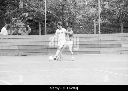 Fußball zwischen Räten und Fußballjournalisten Football, Whizgle News, Dutch Desk, Niederlande, 1950 - 2000 am 04-06-1988. Das Bild enthält diese Themen. Die Szene fängt einen energiegeladenen Moment auf einem Sportplatz ein, geprägt von einer lebhaften und wettbewerbsorientierten Atmosphäre. Im Mittelpunkt stehen zwei junge Spieler, einer in weißer Uniform und der andere in rotem Outfit. Der Spieler in weiß dribbelt geschickt einen Fußball mit einem intensiven Ausdruck, der Entschlossenheit und Konzentration zum Ausdruck bringt. Der Gegner, der rot trägt, befindet sich nahe hinter ihm und versucht, den Ball zu blockieren, was einen Moment o anzeigt Stockfoto