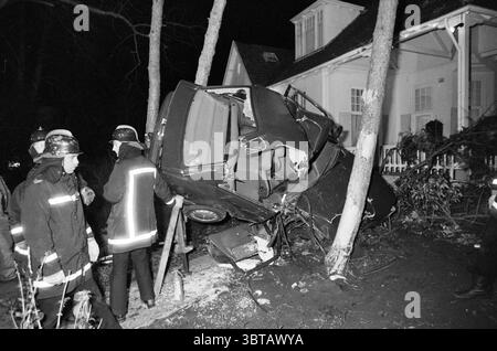 Feuerwehr befreit abgestürzten Wagen von Bäumen., Whizgle News, Dutch Desk, Niederlande, 1950 - 2000 am 05-04-1990. Dies sind die Themen im Bild. In einer Nachtszene ist es zu einem schweren Autounfall gekommen. Zwischen zwei Bäumen befindet sich ein Fahrzeug, dessen Vorderseite angehoben ist, was darauf hindeutet, dass es in die Seite eines Gebäudes gestürzt ist. Die Struktur des Fahrzeugs scheint zerknittert und beschädigt zu sein, was auf die Wucht des Aufpralls hinweist. Feuerwehrleute und Notfallhelfer, in reflektierender Ausrüstung gekleidet, sind im Vordergrund sichtbar, ihre Ausdrücke fokussiert und ernst, während sie die Situation beurteilen Stockfoto