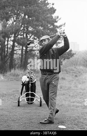 Barry Hughes auf dem Golfplatz Golf Golf Golf Fußball Leute und Trainer, Whizgle News, Dutch Desk, Niederlande, 1950 - 2000 am 13-11-1975. Diese Themen werden in der Abbildung angezeigt. In einer üppigen, grünen Umgebung wird ein Mann mitten im Schwung gefangen und zeigt Konzentration und Konzentration. Er trägt eine Mütze im Vintage-Stil, einen dunklen Pullover und eine taillierte Hose, die die klassische Golfkleidung widerspiegelt. Die Farbpalette besteht aus Erdtönen, mit sattem Grün von Gras und Bäumen, die sich von seiner dunkleren Kleidung abheben. Hinter ihm sitzt eine Golftasche auf einem kleinen Wagen, die auf die Werkzeuge des Sports hinweist. Der Beutel ist f Stockfoto
