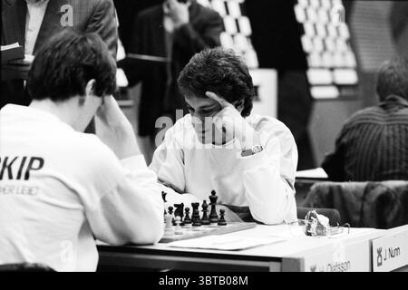 Übersicht über Decathlons H.S.T. [Blastovens Chess Tournament], Whizgle News, Dutch Desk, Niederlande, 1950 - 2000 auf 31-01-1991. Dies sind die Elemente im Bild. Die Szene zeigt ein angespanntes Schachspiel, das in einem Turnier stattfindet. Zwei Spieler sitzen einander gegenüber und konzentrieren sich auf das dazwischen liegende Schachbrett. Ein Spieler, der in einem hellen Langarmshirt gekleidet ist, hat seine Hand zu seinem Tempel erhoben und verkörpert Konzentration und Nachdenklichkeit. Sein Gegner mit dunkleren Haaren in dunklerer Kleidung beugt sich leicht ein, die Augen sind auf dem Brett fixiert und denken über seine nach Stockfoto