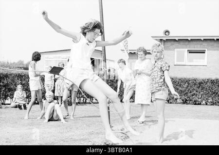 Achtkamp Oosten de Bruijnstraat Sportplatz Ferienspiele Urlaubstage Ferienlager Haarlem Van Oosten de Bruijnstraat Niederlande, Whizgle News, Dutch Desk, Niederlande, 1950 - 2000 am 02-08-1963. Die Abbildung zeigt diese Themen. Die Szene zeigt eine lebhafte Umgebung im Freien, wahrscheinlich in einem Garten oder auf einem Spielplatz. Eine Gruppe von Kindern nimmt an einer Vielzahl von Aktivitäten Teil. Die zentrale Figur, ein Mädchen, das in einem hellen ärmellosen Oberteil und gestreiften Shorts gekleidet ist, scheint mittelgroß zu sein, als sie versucht, ein Seil zwischen zwei Stangen zu lösen, was ein Gefühl von Dynamik und jugendlicher Energie ausstrahlt. Surround Stockfoto