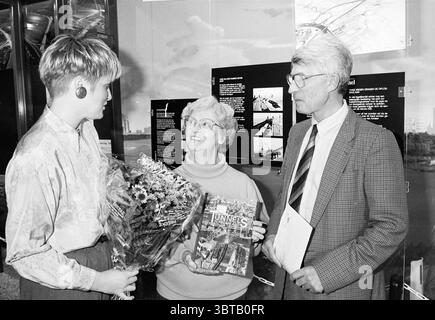 10000. Besucher des Wijkertunnel Informationszentrums, Whizgle News, Dutch Desk, Niederlande, 1950 - 2000 am 19-04-1994. Dies sind die Themen im Bild. In einem gut beleuchteten Innenbereich treffen sich drei Personen in einer engen Gruppe, wodurch eine warme und intime Atmosphäre entsteht. Eine Frau auf der linken Seite, mit kurzen, platinblonden Haaren, trägt große Ohrringe und ein stilvolles Outfit, was auf eine moderne Sensibilität hindeutet. Sie hält einen Blumenstrauß voller lebendiger Blumen, der in Rosa-, Gelb- und Weißtönen gehalten wird, was der Szene einen Hauch Frische verleiht. In der Mitte eine ältere Frau mit kurzem, weißem h Stockfoto