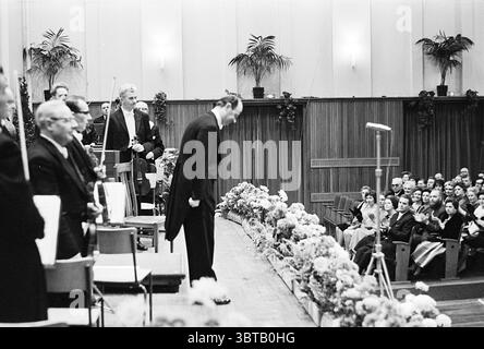 Prinzessin Margriet beim Galakonzert 150 Jahre N.P.O. königliche Empfänge und königliche Besuche des North Holland Philharmonic Orchestra, Whizgle News, Dutch Desk, Niederlande, 1950 - 2000 am 29.11.1963. Die Abbildung zeigt diese Themen. In einer formell gestalteten Umgebung steht ein gut gekleideter Mann an der Front, der sich leicht beugt und einen Moment der Anerkennung oder Dankbarkeit andeutet. Er trägt einen klassischen dunklen Anzug, der ein Gefühl von Zeremonie verkörpert. Um ihn herum befinden sich mehrere Individuen, meist in formeller Kleidung, was auf eine Zusammenkunft von Bedeutung hinweist. Die Szene wird von einer Reihe üppiger Topfpflanzen al. Eingerahmt Stockfoto
