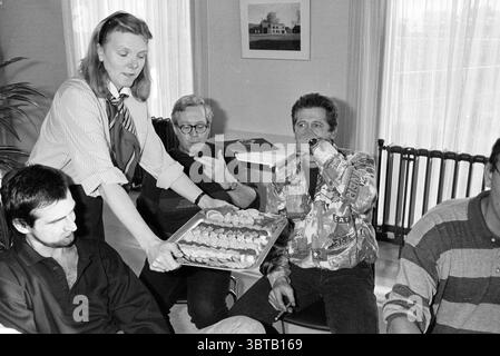 Empfang letzter Drucktag, Whizgle News, Dutch Desk, Niederlande, 1950 - 2000 am 10-10-1993. Das Bild enthält diese Themen. In einem geräumigen Innenbereich versammelt sich eine Gruppe von Männern um einen niedrigen Tisch, um sich zu unterhalten. Die Atmosphäre wirkt entspannt, erfüllt von einem Gefühl von Kameradschaft. Die Wände sind mit minimalistischem Dekor verziert, was auf einen funktionalen, vielleicht gemeinschaftlichen Raum hindeutet. Eine Frau steht zur Seite und präsentiert elegant ein Tablett mit farbenfrohen Vorspeisen, das eine Vielzahl von Texturen und Formen präsentiert. Ihre Kleidung, ein geknöpftes Hemd und eine Krawatte, steht im Kontrast zum Casua Stockfoto