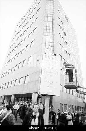 Enthüllung Informationsspalte Heemstede Station Heemstede Niederlande, Whizgle News, Dutch Desk, Niederlande, 1950 - 2000 am 06-02-1994. Diese Themen werden in der Abbildung angezeigt. Die Szene fängt eine geschäftige urbane Umgebung ein, die durch ein modernes Gebäude gekennzeichnet ist, das mit seiner schlanken, reflektierenden Fassade markant aufragt. Das Design des Gebäudes umfasst große, rasterartige Fenster, die einen Eindruck von einem zeitgenössischen architektonischen Stil vermitteln. An vorderster Front versammelt sich eine Vielzahl von Menschen, die verschiedene Altersgruppen und Stile zeigen, die alle in Gesprächen stehen oder auf das Gebäude blicken. Die Einzelpersonen Stockfoto