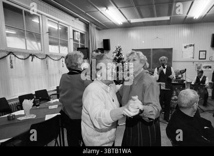 Village House 't Terras Reception Santpoort-Noord Dinkgrevelaan, Whizgle News, Dutch Desk, Niederlande, 1950 - 2000 am 03-01-1997. Diese Themen werden in der Abbildung angezeigt. In einem lebhaften Innenbereich verbringen zwei ältere Frauen einen Moment der Freude, während sie zusammen tanzen. Ihre Ausdrucksformen strahlen Glück und Nostalgie aus, umrahmt von dem warmen Leuchten der weichen Deckenbeleuchtung, die dem Raum eine gemütliche Atmosphäre verleiht. Die Wände sind mit festlichen Dekorationen geschmückt, die auf eine Feier hinweisen, vielleicht um die Weihnachtszeit herum, mit einem geschmückten Weihnachtsbaum, der majestätisch im Hintergrund steht. Die Szene ist Bus Stockfoto