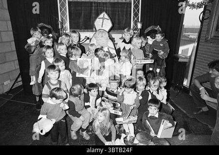 Sinterklaas im Haarlems Dagblad Haarlems Dagblad etc. Und IJmuider Courant und Koeri St. Nicolaas Sinterklaas, Whizgle News, Dutch Desk, Niederlande, 1950 - 2000 am 01-12-1982. Dies sind die Elemente im Bild. In einem festlichen Innenbereich versammelt sich eine große Gruppe von Kindern um eine zentrale Figur, die als traditioneller heiliger gekleidet ist. Der heilige, der mit einem langen Gewand und einem prominenten Hut geschmückt ist, sitzt auf einem Stuhl und strahlt ein Gefühl von Wärme und Autorität aus. Um ihn herum gibt es zahlreiche Kinder, alle mit unterschiedlichen Ausdrucksformen, die von Begeisterung bis Neugier reichen. Die Kinder sind eine Mischung aus Alter und Größe, Stockfoto