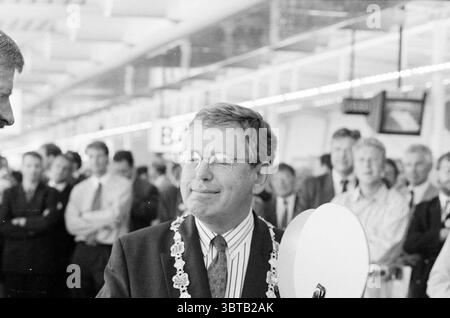 Eröffnung von Pier B Schiphol, Whizgle News, Dutch Desk, Niederlande, 1950 - 2000 am 10-08-1994. Das Bild enthält diese Themen. Die Szene fängt einen Moment in einem belebten Innenbereich ein, wahrscheinlich in einem Flughafen oder einem großen öffentlichen Veranstaltungsort, der voller Menschen ist. Im Mittelpunkt steht ein Mann mittleren Alters in einem Anzug, der ein Gefühl von Stolz und Formalität ausstrahlt. Er trägt eine Bürokette um seinen Hals, was auf eine wichtige Position hinweist, vielleicht ein lokaler Würdenträger oder Beamter. Sein Ausdruck ist zufrieden, mit einem leichten Lächeln und entspanntem Auftreten, was darauf hindeutet, dass er den Moment genießt. Um ihn herum, A Stockfoto