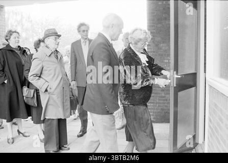 Lift für ältere Menschen Luxemburgstraat Lifts Haarlem Luxemburgstraat Niederlande, Whizgle News, Dutch Desk, Niederlande, 1950 - 2000 am 18-05-1987. Dies sind die Elemente im Bild. In einem belebten Eingangsbereich versammelt sich eine Gruppe von Einzelpersonen, was auf eine lebhafte Veranstaltung oder Zusammenkunft hindeutet. Im Vordergrund steht eine ältere Frau, die in einer dunklen, strukturierten Samtjacke und einem Rock gekleidet ist, auf das Aufschließen einer Tür, deren Ausdruck Konzentration ist. Sie trägt eine Brille und ihre Haare sind ordentlich gestylt. Begleitet wird sie von einem Mann in einem hellen Anzug, der sich leicht beugt, während er den Schlüssel übergibt, bereit Stockfoto