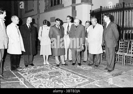 Bischof Bomers besucht St. Bavo Churches Roman Catholic Church, Whizgle News, Dutch Desk, Niederlande, 1950 - 2000 am 20.05.1984. Das Bild enthält diese Themen. Die Szene zeigt eine Gruppe von Männern und einer Frau, die sich in einem Innenhof oder einem Außenbereich versammelt haben, wahrscheinlich Teil eines Ziegelbaus oder eines Steingebäudes. Die Einstellung hat eine formale Atmosphäre, die von der Kleidung der einzelnen Personen vorgeschlagen wird. Viele tragen lange, helle Mäntel, während ein Mann in einem Anzug erscheint, was auf eine Versammlung für einen wichtigen Zweck hindeutet. Die Gruppe beschäftigt sich mit der Beobachtung eines großen, komplizierten Wandteppichs oder Kunstwerks auf dem Grou Stockfoto