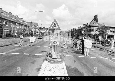 Verkehrsbrigade Rijksstraatweg Verkehrssicherheit Haarlem Rijksstraatweg Niederlande, Whizgle News, Dutch Desk, Niederlande, 1950 - 2000 am 26-08-1985. Die Abbildung zeigt diese Themen. Die Szene fängt eine ruhige Straße ein, flankiert von Wohngebäuden mit unterschiedlichen architektonischen Stilen, die ein Gefühl für eine Vorstadtgegend vermitteln. Die Strukturen zeigen eine Mischung aus hellen und dunklen Ziegeltönen, und einige verfügen über Giebeldächer, die der Umgebung Charakter verleihen. Im Vordergrund ist an der Straße ein Straßenübergang deutlich abgegrenzt, der bis auf wenige Fußgänger meist leer ist. Der Querweg ist markiert mit Stockfoto