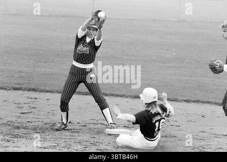 Softball: Terrasvogels - Twins, Whizgle News, Dutch Desk, Niederlande, 1950 - 2000 am 19.08.1990. Diese Themen sind in der Abbildung dargestellt. Die Szene fängt einen dynamischen Moment auf einem Softballfeld ein, in dem zwei Spieler ein intensives Spiel führen. Der Athlet auf der linken Seite ist zielgerichtet und trägt eine auffällige gestreifte Uniform mit dunklen und hellen Linien. Sie befindet sich in einer fesselnden Haltung, die Arme sind nach oben gestreckt, während sie sich auf einen Ball vorbereitet. Ihr Ausdruck vermittelt Entschlossenheit und Konzentration, betont durch ein Visier, das ihre Augen vor der Sonne schützt. In der Zwischenzeit, rechts, ein Spieler sl Stockfoto