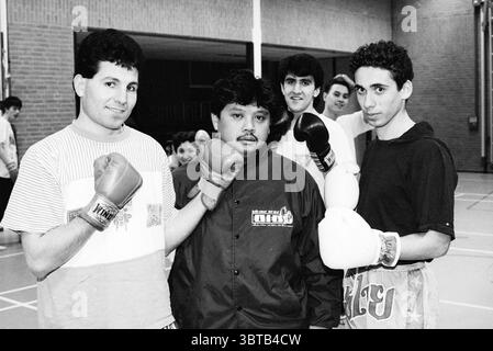 Jerry Smit Pentjak Silat Hoofddorp The Netherlands, Whizgle News, Dutch Desk, Niederlande, 1950 - 2000 am 25-02-1992. Die Abbildung zeigt diese Themen. In einem geräumigen Indoor Gym werden mehrere Personen versammelt, was eine lebhafte Atmosphäre schafft. Die Einrichtung verfügt über einen polierten Holzboden, helle Wände und einen Hauch von natürlichem Licht, das durch große Fenster filtert, was ein helles, aber leicht gedämpftes Ambiente bietet. Im Vordergrund stehen zwei junge Männer mit markanten Frisuren. Eine hat eine dunkle, leicht lockige Mähne und trägt rote Boxhandschuhe, während die andere mit einer mehr stru ist Stockfoto