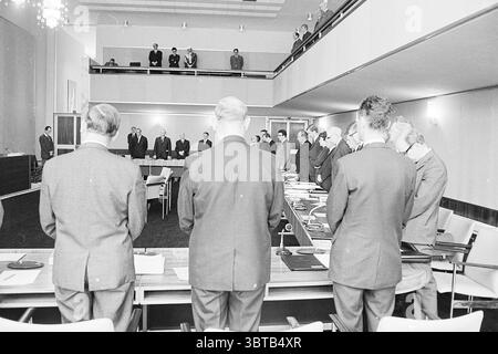 Gedenken an Mr. Bührman Commemories, Whizgle News, Dutch Desk, Niederlande, 1950 - 2000 am 25-11-1968. Dies sind die Elemente im Bild. Die Szene zeigt eine formelle Versammlung in einem geräumigen, modernen Konferenzraum. Der Raum verfügt über einen langen rechteckigen Tisch, poliert und gut organisiert, auf dem verschiedene Dokumente und Gegenstände ordentlich angeordnet sind. Im Vordergrund stehen mehrere Individuen mit dem Rücken zum Betrachter, alle in dunklen Anzügen gekleidet, was auf ein professionelles oder staatliches Umfeld hindeutet. Ihre Haltung vermittelt ein Gefühl von Ernsthaftigkeit und Respekt, was darauf hindeutet Stockfoto