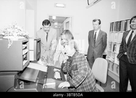 Eröffnung der Station Haarlem Eröffnung der Öffnungen Inbetriebnahme Station Haarlem Niederlande, Whizgle News, Dutch Desk, Niederlande, 1950 - 2000 am 11-05-1989. Diese Themen sind in der Abbildung dargestellt. In einer monochromatischen Umgebung versammelt sich eine Gruppe von Individuen um ein Retro-Computerterminal, das auf den Bildschirm fokussiert ist. Zwei Personen, eine in einem gemusterten Blazer und eine andere in einem formelleren Anzug, lehnen sich eng an, ihre Ausdrucksformen sind eine Mischung aus Neugier und Konzentration. Die Person in dem gemusterten Blazer scheint in der Bedienung zu sein, möglicherweise tippen oder die Steuerelemente des Computers verwenden. Hinter dem Stockfoto