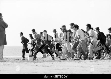 IJmond MTS 700 Students Beach Run, Whizgle News, Dutch Desk, Niederlande, 1950 - 2000 am 18-10-1993. Diese Themen sind in der Abbildung dargestellt. Eine Gruppe von Läufern wird mitten im Schritt aufgenommen und erzeugt eine dynamische Szene voller Energie und Bewegung. Die in verschiedenen Sportbekleidung gekleideten Individuen zeigen eine bunte Farbmischung, von leuchtenden Rot- und Blautönen bis hin zu gedämpften Grau- und Weißtönen. Die Läufer sind in einer gestaffelten Formation positioniert, was einen Start in ein Rennen suggeriert und das Gefühl der Dringlichkeit in der Komposition verstärkt. Der Hintergrund zeigt eine sanfte Küstenlinie, auf die sich das Meer ausdehnt Stockfoto