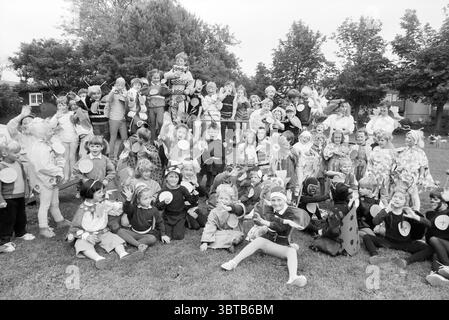 Insecte Afternoon Brederoschool Santpoort Schools Santpoort, Whizgle News, Dutch Desk, Niederlande, 1950 - 2000 am 25-06-1987. Das Bild enthält diese Themen. Die Szene zeigt ein lebhaftes Zusammenkommen von Kindern in einem Park mit festlicher und verspielter Atmosphäre. Eine große Gruppe von Kindern, alle in lebendigen Kostümen gekleidet, füllt den Vordergrund. Viele Kostüme haben kreative Designs, die von verschiedenen Themen wie Tieren, Blumen und klassischen Zeichentrickfiguren inspiriert sind, wobei leuchtende Farben wie Rot, Gelb, Blau und Grün die visuelle Palette dominieren. Die Umgebung ist ein offener, grasbewachsener Bereich, der von begrenzt wird Stockfoto