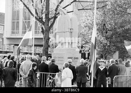 Silent Journey IJmuiden IJmuiden the Netherlands, Whizgle News, Dutch Desk, Niederlande, 1950 - 2000 am 03-05-1993. Das Bild enthält diese Themen. In der Mitte steht ein großes Steindenkmal, das zwei feierliche Gestalten in Gewändern zeigt. Die Statue zeichnet sich durch ihren grauen Farbton und die komplizierten Details aus, die ein Gefühl von Schwerkraft und Erinnerung vermitteln. Um das Denkmal herum hat sich eine Menschenmenge versammelt, ihre Kleidung ist vielfältig im Stil, aber weitgehend gedämpft in der Farbe, die eine respektvolle Stimmung widerspiegelt. Die Einzelpersonen sind eng zusammen positioniert und erscheinen in Verachtung verwickelt Stockfoto