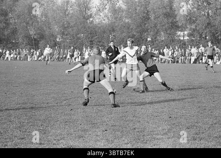 Kennemeren - dem Football, Whizgle News, Dutch Desk, Niederlande, 1950 - 2000 am 19.10.1969. Diese Themen werden in der Abbildung angezeigt. Die Szene zeigt ein lebhaftes Fußballspiel auf einem grasbewachsenen Feld, das sich unter klarem Himmel ausdehnt. Das üppige grüne Gras bildet einen scharfen Kontrast zur Kleidung der Spieler, die aus hellen und dunklen Trikots besteht. Eine Gruppe von Athleten ist in einem dynamischen Moment beschäftigt, wobei ein Spieler in weiß auf den Ball sprintet, die Arme weit ausgebreitet sind, während er um zwei Gegner in dunkleren Farben manövriert. Die Spieler strahlen Energie und Entschlossenheit aus, ihr fokussierter Ausdruck Stockfoto