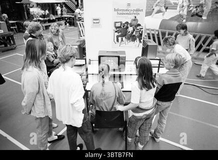 Stuif-Stuif Beijneshal Stuif Haarlem the Netherlands, Whizgle News, Dutch Desk, Niederlande, 1950 - 2000 am 05-08-1985. Diese Themen sind in der Abbildung dargestellt. Eine Gruppe von Kindern versammelt sich um einen Computer in einer belebten Umgebung, wahrscheinlich in einer Schule oder einem Gemeindeevent. Die Szene ist voller jugendlicher Energie und Neugier. Die Kinder, sowohl Jungen als auch Mädchen, tragen lässige Kleidung, die typisch für das Ende des 20. Jahrhunderts ist, mit Farben, die von hellen Tönen bis zu gedämpften Tönen reichen. Einige tragen übergroße Pullover, Shorts und Jeans, während andere mit farbenfrohen T-SH aufwarten Stockfoto