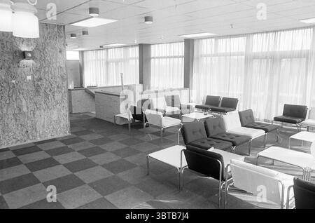 Int. Schwester Wohnung Diaconessenhuis Interior, Whizgle News, Dutch Desk, Niederlande, 1950 - 2000 am 12-04-1973. Das Bild enthält diese Themen. Die Szene zeigt eine geräumige Inneneinrichtung, die sich durch ein modernes, minimalistisches Design auszeichnet. Das Licht strömt durch große Fenster, die mit weißen Vorhängen verziert sind, und schafft eine helle und luftige Atmosphäre. Die Wände sind überwiegend in einem hellen, neutralen Ton, möglicherweise hellgrau oder beige, ergänzt durch eine strukturierte Steinwand, die Tiefe und einen Hauch von Eleganz verleiht. Der Boden ist gemustert und wechselt zwischen dunklem und hellem squa Stockfoto