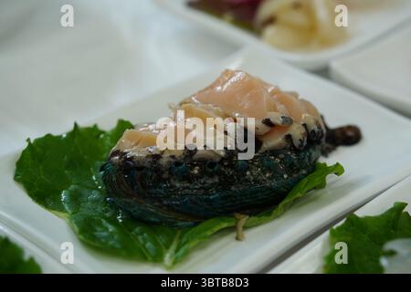 Frische Abalone-Sashimi-Scheiben auf weißer Platte mit grünem Blatt Stockfoto