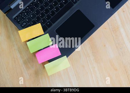 Leere saubere bunte Aufkleber auf dem Laptop über Holztischhintergrund. Zur Informationserinnerung. Ein Stück Papier. Platz Für Text. Stockfoto