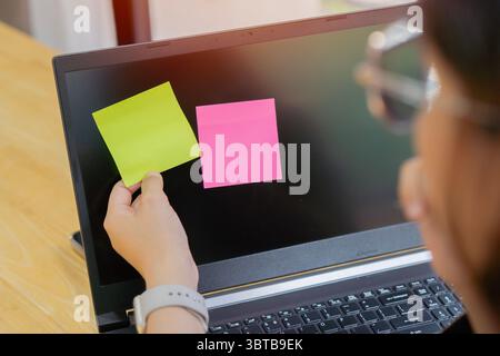 Rückansicht der Hände einer Frau, die Haftnotizen auf dem Laptop kleben. Kopierbereich. Brainstorming-Konzept. Stockfoto