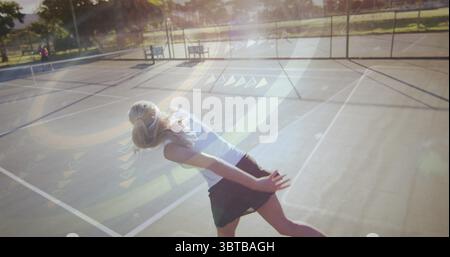 Eine gewölbte Tennisspielerin wirft zur goldenen Stunde den Ball im Netz auf dem Platz hoch, Linsenfackeln Stockfoto