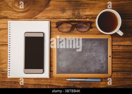Zeigt einen flachen Schreibtisch mit Pad und Smartphone, gerahmte Tafel, Gläser, Kaffee, Stift Stockfoto