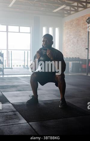 Afroamerikaner in Sportbekleidung, der Kettlebell in der Turnhalle mit Langhanteln und Tellern aufführt Stockfoto