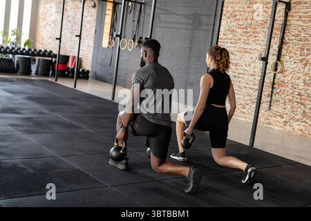 Verschiedene Trainingspartner, die sich in Sportbekleidung mit Kettlebells im Fitnessstudio mit Ringen ausruhen Stockfoto