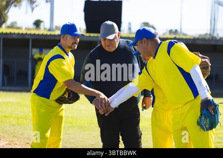 Baseballtrainer und männliche Spieler drängen sich, bevor sie das Spiel mit Handschuhen auf dem Rasenfeld beginnen Stockfoto