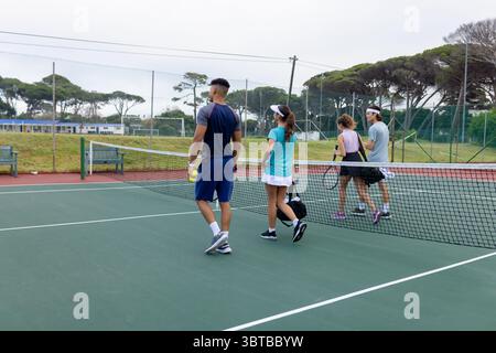 Verschiedene Freunde laufen über das Tennisnetz auf dem Tennisplatz im Freien mit Schlägern, Bälle und Tasche Stockfoto