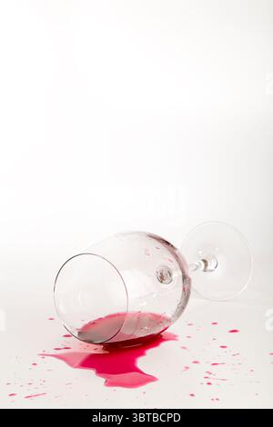Gefallenes Rotweinglas verschütteter Wein auf Tisch auf weißem Hintergrund Stockfoto