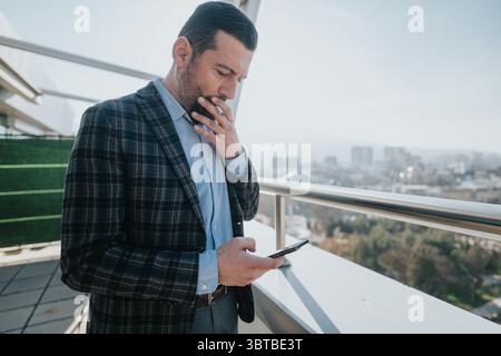 Professioneller Mann mit Smartphone auf einem Balkon mit Blick auf die Stadtlandschaft Stockfoto