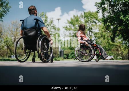 Zwei Personen im Rollstuhl, die einen sonnigen Tag im Park genießen, umgeben von üppigen grünen Bäumen. Stockfoto