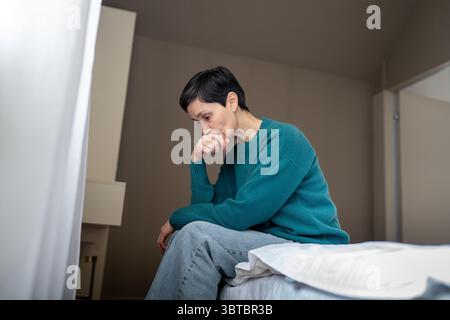 Traurige, überforderte Frau in Verzweiflung auf dem Bett, die nach unten starrt. Angst vor Menschen, nervöses Weibchen Stockfoto