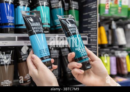 Poznan, Polen – 30. Juni 2025: Nahaufnahme der Hände, die hellblaue und türkisfarbene Acrylfarben halten und die Auswahl an Kunstmaterialien für kreative Zwecke hervorheben Stockfoto