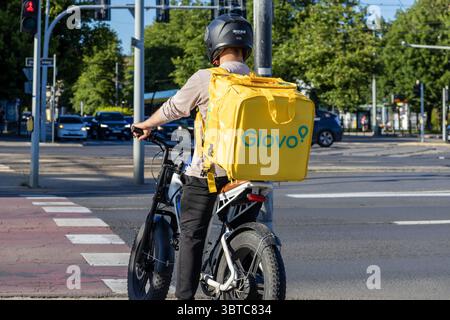 Posen, Polen - 30. Juni 2025: Ein Glovo-Kurier auf einem E-Bike mit gelbem Thermorucksack wartet an der geschäftigen Stadtüberquerung Stockfoto