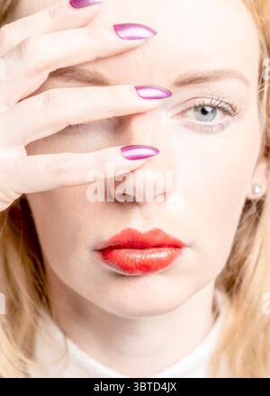 Eine Frau mit rotem Lippenstift bedeckt ihre Augen mit der Hand und zeigt ihren lila nagellack. Stockfoto