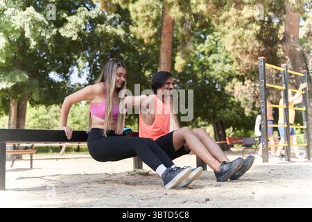 Fitnesspaare, die auf einer Bank in einem lebhaften Calisthenics-Park tauchen, einen sonnigen Tag genießen und gleichzeitig Kraft und Koordination verbessern Stockfoto