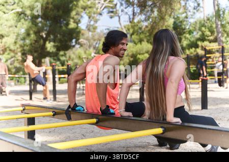 Mann und Frau trainieren gemeinsam, spielen in einem lebhaften Calisthenics-Park Dips an parallelen Bars und genießen einen aktiven Sommertag Stockfoto