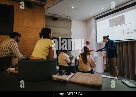 Teammitglieder in einem Besprechungsraum arbeiten zusammen, während sie Daten auf einem Projektor präsentieren und Teamarbeit und Kommunikation in einer vielfältigen Umgebung präsentieren Stockfoto
