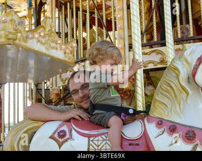 Vater und Sohn, die gemeinsam in san sebastian, spanien, auf einem Karussell reiten und einen Sommertag im Vergnügungspark genießen Stockfoto