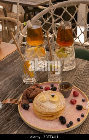 Eine gemütliche Frühstücksszene mit flauschigen Pfannkuchen mit frischen Beeren und Bananenscheiben, serviert neben Eistee und Espresso, die an Comf erinnern Stockfoto