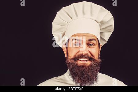Glücklicher Koch, junger Mann mit Bart, lächelnd. Kochmütze. Bärtige Köche, Köche oder Bäcker positiv. Porträt eines glücklichen Küchenchefs Stockfoto