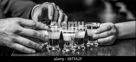 Hände, die auf einer Bar Gläser schießen. Cocktailset. Männliche Hände grüßen mit Gläsern Wodka und Likör. Beste Freunde, die mit ihnen Toast machen Stockfoto